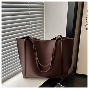 Detail of a large brown leather tote bag with dual straps in a sunny, modern setting