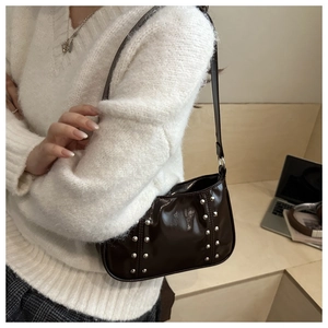 Detail of dark brown patent leather baguette bag with silver rivets on model shoulder