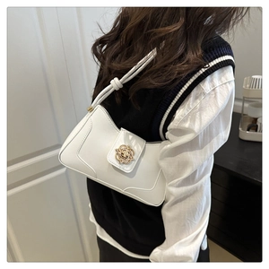 Close-up of a white leather underarm bag featuring a gold floral clasp and knotted strap