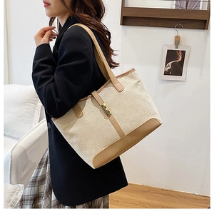 Detail of color-block canvas and leather tote showing golden lock and reinforced corners
