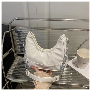 Close-up of white patent leather crescent bag with silver chain and wide strap detail