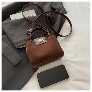 Coffee brown suede tote bag with metal handle placed on grey suit fabric