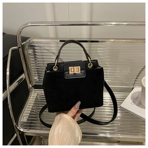Detail of black patchwork leather handbag with gold metal lock on modern chair