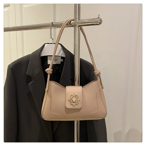 Détail d'un sac baguette chic beige avec fermoir fleuri doré sur un cintre blanc
