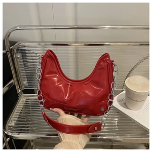 Close-up of red glossy patent leather crescent bag with decorative silver metal chains