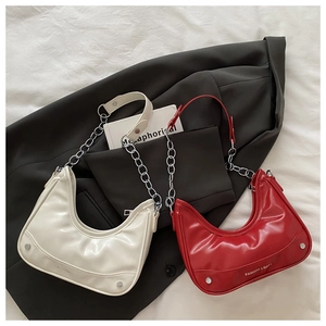 Detail of glossy patent leather half-moon bags in beige and red with silver chain straps