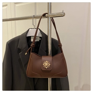Détail du sac à main en cuir marron foncé avec boucle florale dorée sur fond de costume chic