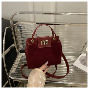 Detail of burgundy faux suede handbag featuring gold metallic twist lock and ring handle