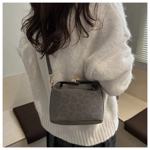Detail of grey leopard print crossbody bag with metal lock worn on white knit sweater