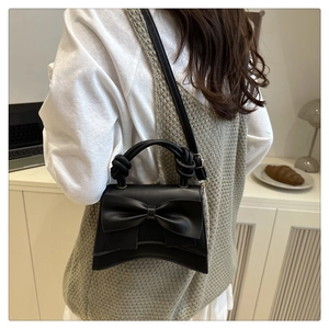Close-up of black matte handbag featuring a large leather bow and twisted rope handle