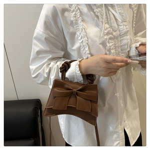 Close-up of a brown bow handbag with a unique knotted handle worn with a white blouse
