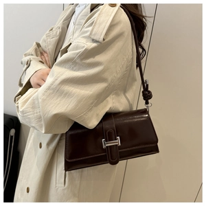 Detail of a dark brown glossy leather shoulder bag with a silver metallic buckle and knot strap