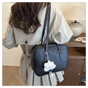 Detail of minimalist black faux leather shoulder bag with a white plush cloud charm on model