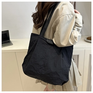 Detail of black pleated tote bag with fashion label worn on shoulder in a home setting