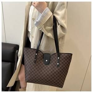 Detail view of large brown tote bag with M-letter print and black leather shoulder straps