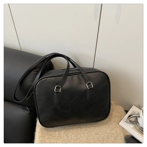 Detail of minimalist black matte leather Boston bag with silver hardware on a sofa