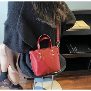 Close-up of red patent leather bucket bag with gold rivets and adjustable shoulder strap