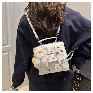 Close-up of white mini backpack featuring colorful B letter print and plush bear charm