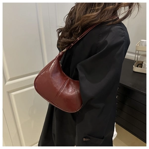 Close-up of a burgundy oil wax leather crescent bag worn on a woman shoulder