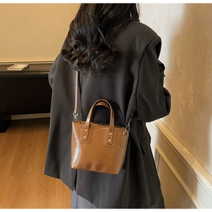 Brown leather bucket bag with gold rivets shown as a crossbody on a female model