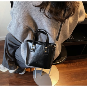 Detail of a chic black glossy leather tote bag with rivets and crossbody strap