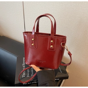 Detail of dark red glossy leather handbag featuring golden studs and detachable shoulder strap