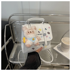 Close-up of white PU leather bag with print and cute plush bear charm on metal shelf