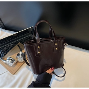 Close-up of a dark brown glossy leather handbag with gold rivets and dual handle detail