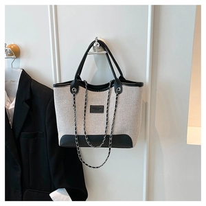 Bolso tote de gran capacidad en lona beige con ribetes negros y detalle de cadena