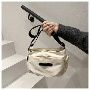 Close-up of cream nylon crossbody bag with black strap and side pocket detail