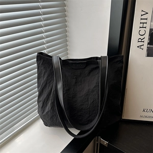Minimalist black textured nylon tote bag with fashion label shown in natural window light
