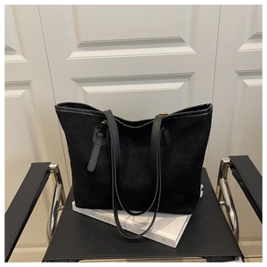 Détail du grand sac cabas noir en daim avec fines anses sur une chaise en métal noir