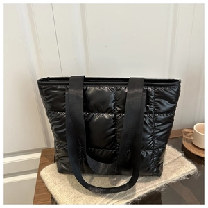 Detail of black quilted tote bag with padded grid pattern and wide fabric straps