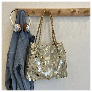 Close-up of golden sequin tote bag with metallic logo plate and braided handle detail