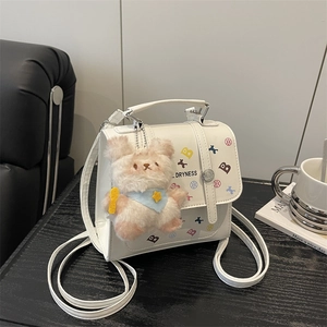 White faux leather backpack with colorful prints and a plush bunny charm on table
