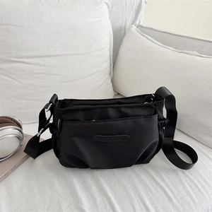 Minimalist black nylon crossbody bag with multi-layer zippers and side pockets on a sofa