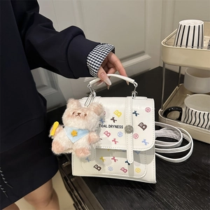 White printed crossbody bag with colorful letters and a plush bear pendant on a table