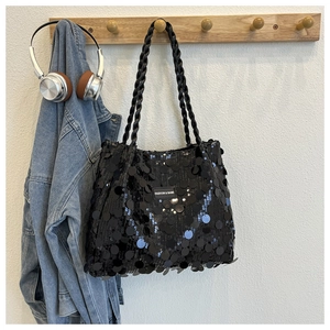 Detailed close-up of shiny black sequin handbag texture with woven handle and fashion label