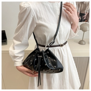 Detailed shot of a black leather bucket bag with silver studs worn as a crossbody bag