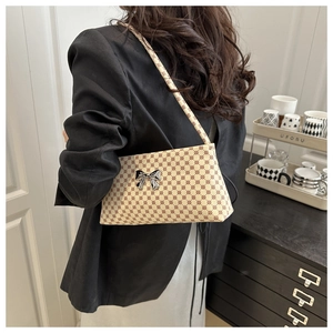 Detail of vintage beige shoulder bag with geometric print and silver bow worn by a model