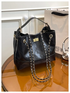 Detail of black quilted leather handbag with gold twist lock and chain strap on table