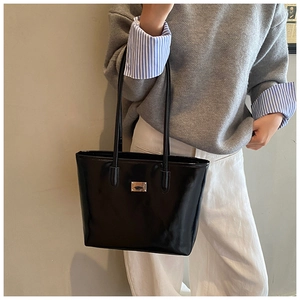 Detail of glossy black tote bag featuring a metallic logo and sleek patent leather texture