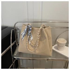 Detail of a beige tote bag with woven handles and blue silk scarf on a metal cart