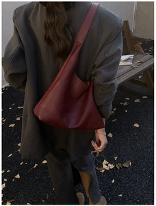 Detail of a deep red large leather tote bag worn with a grey suit in an autumn setting