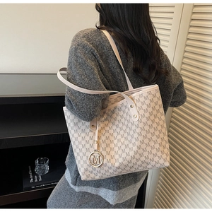 Detail of a large beige tote bag with M-pattern print and metallic charm on a model