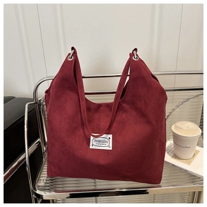 Detail of burgundy faux suede tote bag with metal eyelets and fashion label on shelf