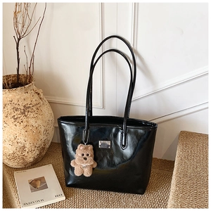 Close-up of black glossy leather tote bag with a cute brown plush bear charm and metal tag