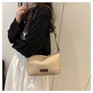Détail du sac à bandoulière en toile beige avec écusson cuir et sangle réglable