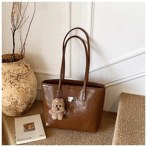 Detail of a brown glossy leather tote bag featuring a cute teddy bear charm and silver tag