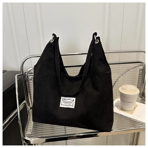 Detail of black suede tote bag with fashion label on a minimalist silver shelf